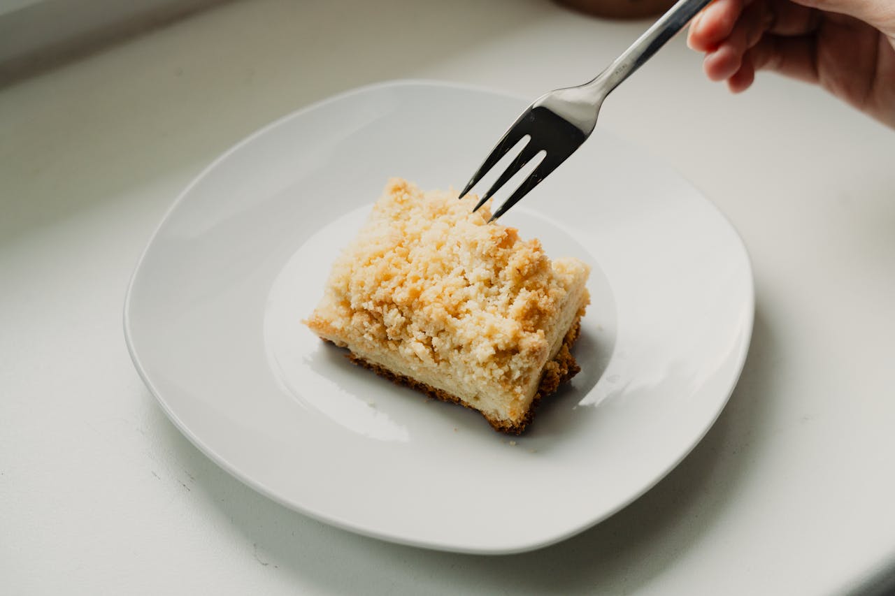 Close-up of a piece of streuselkuchen on a white plate with a fork poised to take a bite.