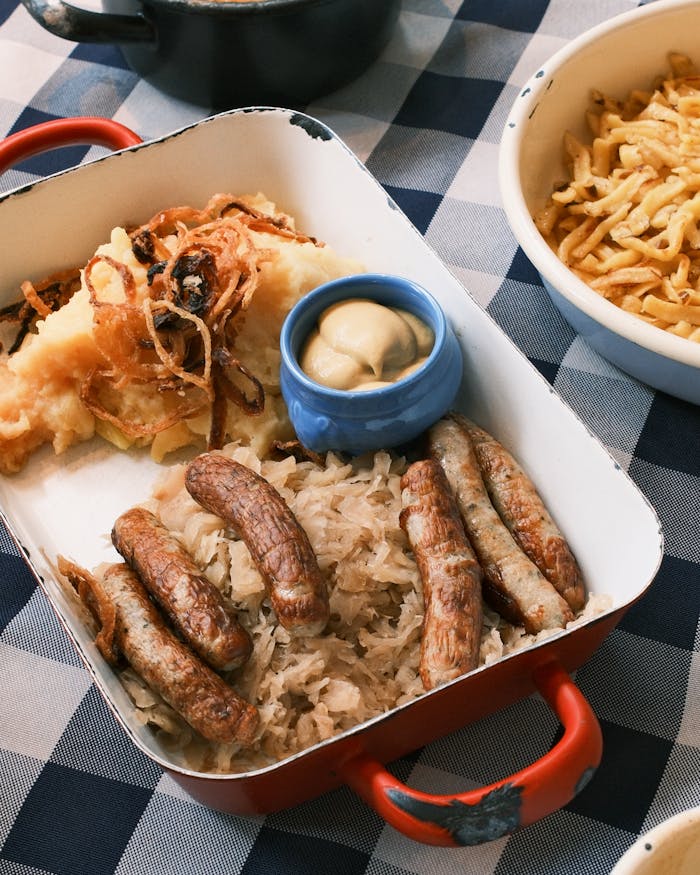 Delicious German sausages served with sauerkraut, mashed potatoes, and mustard on a blue checkered tablecloth.