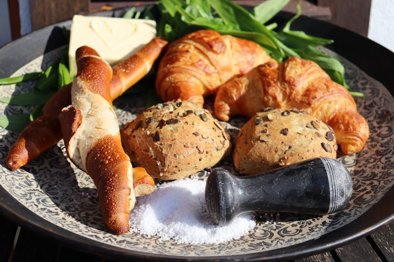 A selection of fresh breads including croissants and pretzels served with butter and salt.